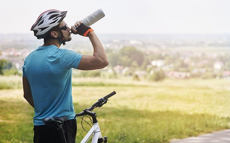 fietser die met zijn fiets in een veld staat en water drinkt uit zijn bidon