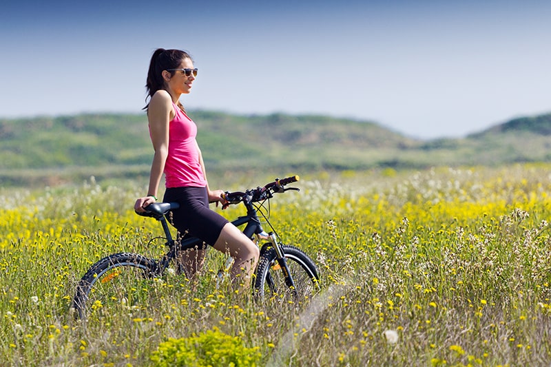 een meisje zittend op een fiets midden in een veld met gele bloemen